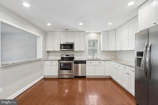 kitchen featuring appliances with stainless steel finishes, sink, white cabinets, light stone countertops, and dark wood-type flooring