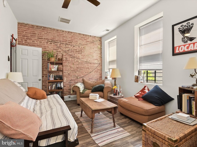 living room featuring hardwood / wood-style flooring, ceiling fan, and brick wall