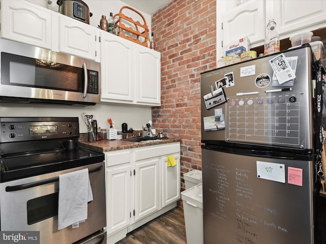 kitchen with appliances with stainless steel finishes, brick wall, dark wood-type flooring, sink, and white cabinets