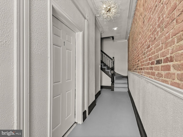 hallway featuring crown molding, brick wall, a textured ceiling, and an inviting chandelier