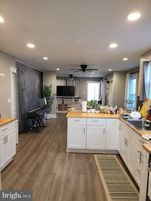 kitchen with butcher block countertops, sink, white cabinets, and dark wood-type flooring