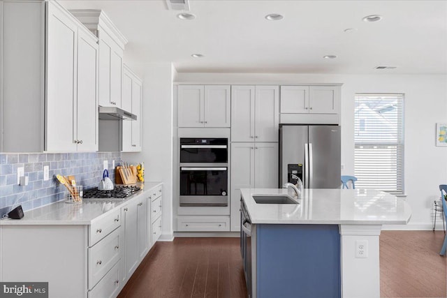 kitchen with a center island with sink, appliances with stainless steel finishes, decorative backsplash, white cabinets, and sink