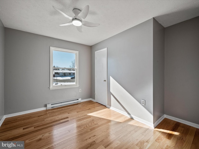 spare room featuring ceiling fan, a baseboard heating unit, light wood-type flooring, and a textured ceiling