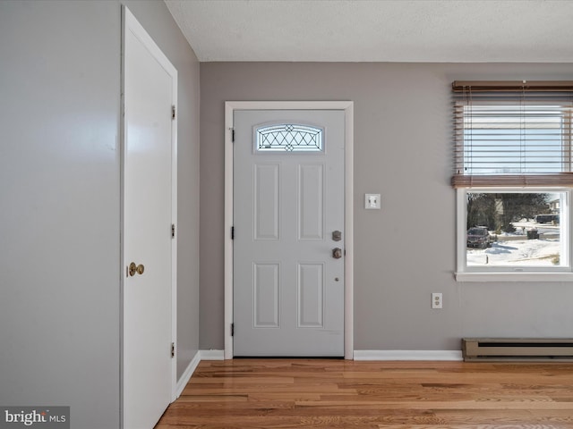 foyer entrance featuring a baseboard heating unit, light wood-type flooring, and a healthy amount of sunlight