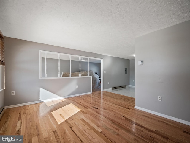 spare room featuring baseboard heating, light wood-type flooring, and a textured ceiling