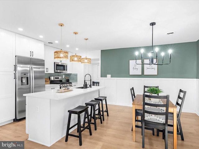 kitchen featuring pendant lighting, sink, light hardwood / wood-style floors, stainless steel appliances, and a center island with sink