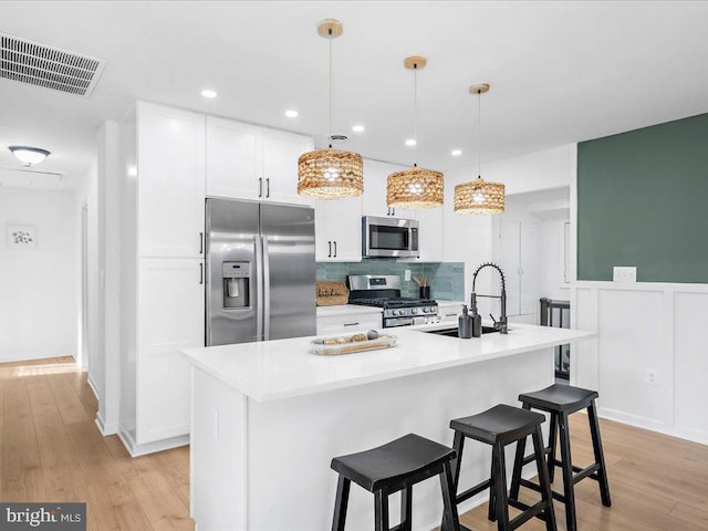 kitchen featuring appliances with stainless steel finishes, sink, an island with sink, and hanging light fixtures