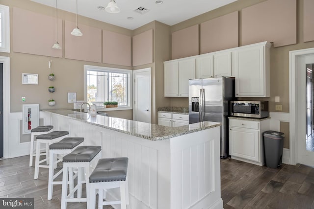 kitchen with white cabinetry, light stone countertops, kitchen peninsula, decorative light fixtures, and appliances with stainless steel finishes