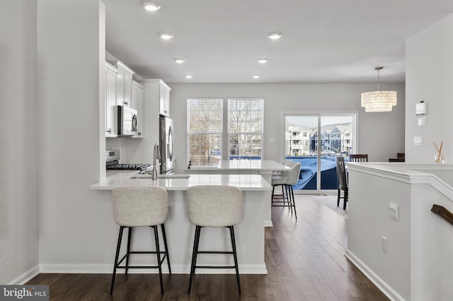 kitchen featuring sink, white cabinetry, a kitchen breakfast bar, pendant lighting, and stainless steel appliances