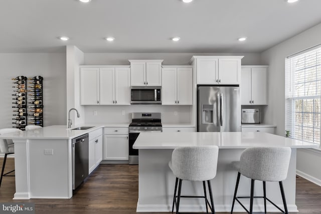 kitchen with appliances with stainless steel finishes, sink, white cabinets, a kitchen bar, and a center island