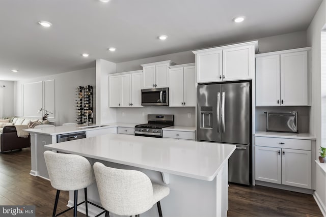 kitchen featuring appliances with stainless steel finishes, sink, white cabinets, a kitchen breakfast bar, and kitchen peninsula