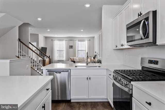 kitchen featuring appliances with stainless steel finishes, dark hardwood / wood-style floors, white cabinetry, sink, and kitchen peninsula