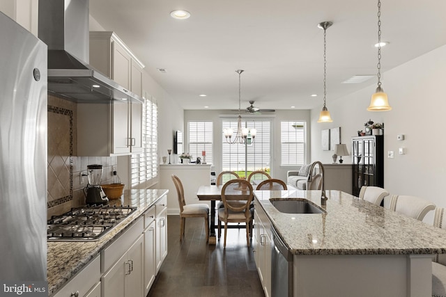 kitchen featuring a center island with sink, pendant lighting, wall chimney range hood, and sink