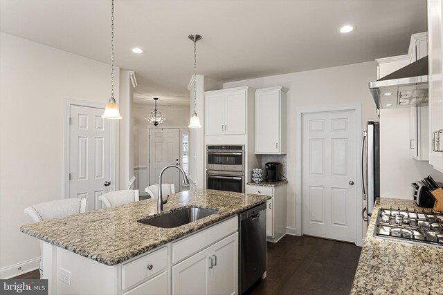 kitchen with light stone countertops, appliances with stainless steel finishes, sink, white cabinets, and an island with sink