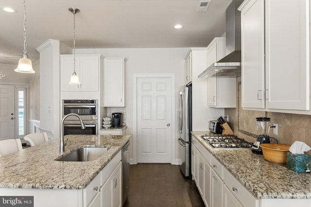 kitchen featuring backsplash, a center island with sink, wall chimney exhaust hood, decorative light fixtures, and white cabinetry