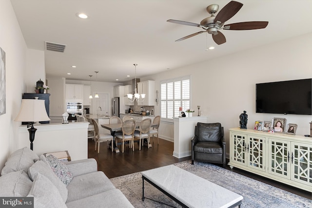 living room featuring dark hardwood / wood-style flooring, ceiling fan with notable chandelier, and sink