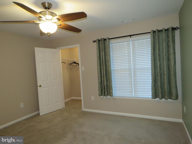 unfurnished bedroom with a spacious closet, a closet, ceiling fan, and light carpet