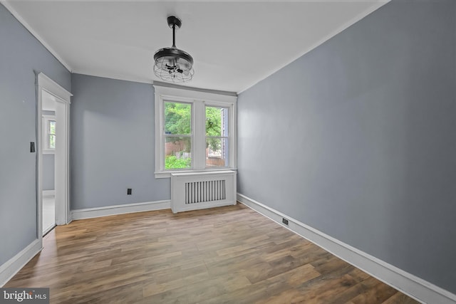 empty room featuring wood-type flooring, ornamental molding, and a notable chandelier