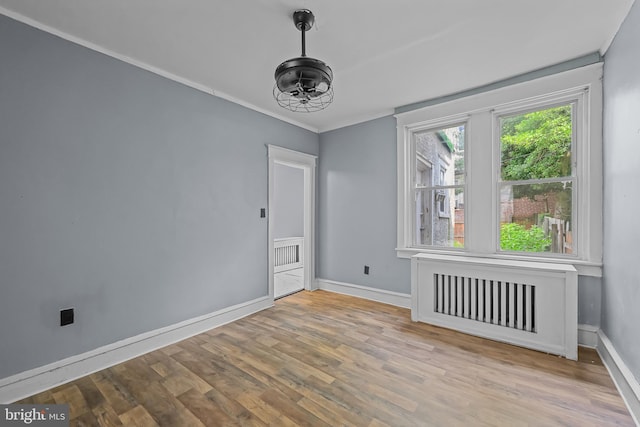 empty room featuring radiator heating unit, light hardwood / wood-style floors, and ornamental molding