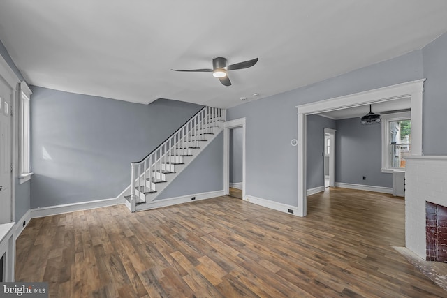 unfurnished living room featuring ceiling fan, dark hardwood / wood-style floors, and a brick fireplace