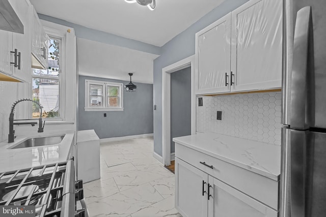 kitchen featuring stainless steel fridge, light stone counters, sink, decorative light fixtures, and white cabinets