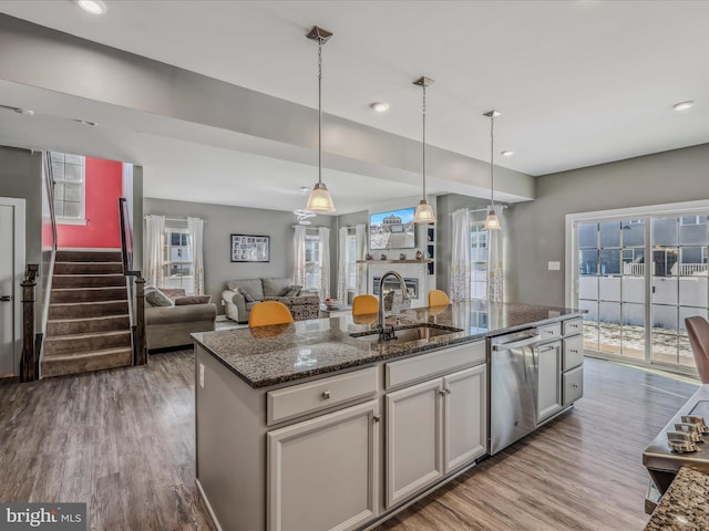 kitchen featuring pendant lighting, dishwasher, dark stone counters, sink, and a center island with sink