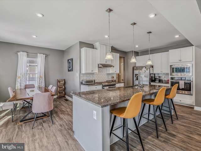 kitchen with white cabinetry, appliances with stainless steel finishes, a spacious island, a kitchen breakfast bar, and sink