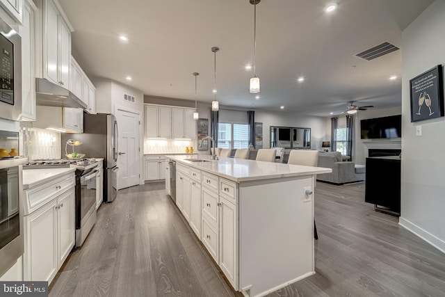 kitchen with appliances with stainless steel finishes, decorative light fixtures, sink, white cabinets, and a center island with sink