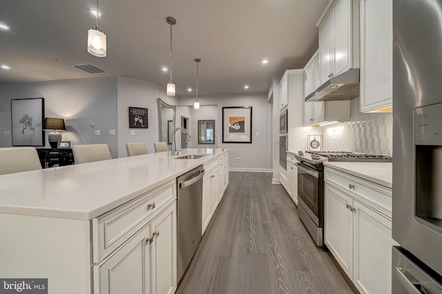 kitchen with decorative light fixtures, sink, white cabinets, stainless steel appliances, and a spacious island