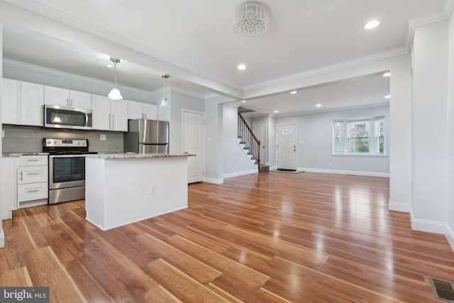 kitchen with a kitchen island, appliances with stainless steel finishes, white cabinets, backsplash, and hanging light fixtures