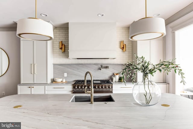 kitchen with decorative backsplash, light stone counters, custom exhaust hood, white cabinets, and hanging light fixtures