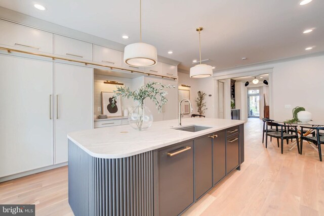 kitchen featuring a kitchen island with sink, white cabinetry, sink, and hanging light fixtures