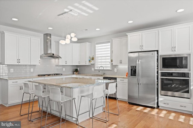 kitchen featuring stainless steel appliances, white cabinetry, and wall chimney exhaust hood