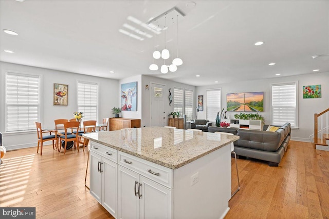 kitchen with white cabinets, pendant lighting, light hardwood / wood-style floors, and a center island