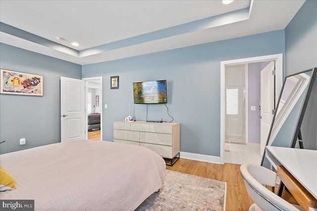 bedroom featuring ensuite bathroom, a raised ceiling, and light wood-type flooring