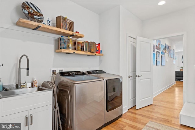 clothes washing area with cabinets, washing machine and clothes dryer, light hardwood / wood-style floors, and sink