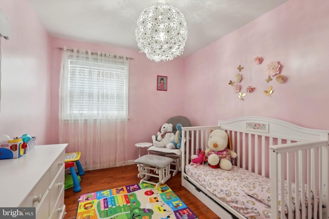 bedroom with dark hardwood / wood-style flooring, a nursery area, and an inviting chandelier