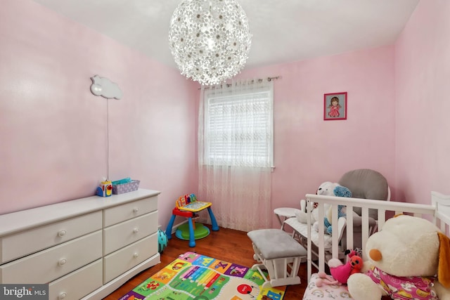 bedroom featuring a crib, dark hardwood / wood-style floors, and a notable chandelier