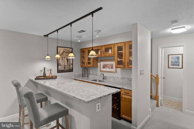 kitchen featuring kitchen peninsula, light stone countertops, sink, and decorative light fixtures