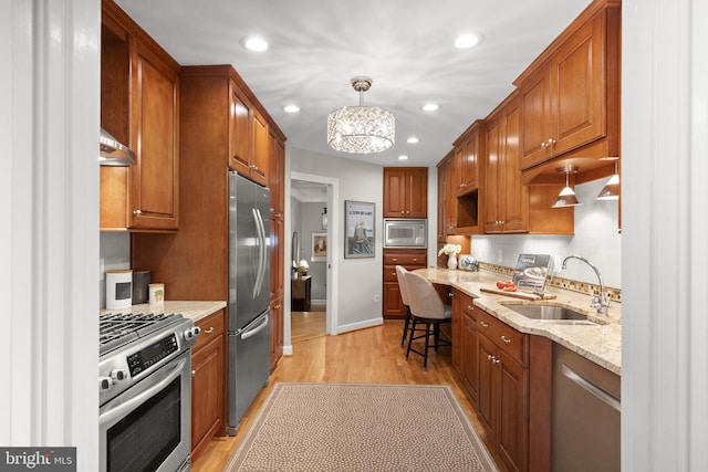 kitchen featuring sink, light hardwood / wood-style flooring, light stone countertops, appliances with stainless steel finishes, and decorative light fixtures