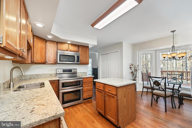 kitchen with appliances with stainless steel finishes, sink, hanging light fixtures, a center island, and light hardwood / wood-style flooring