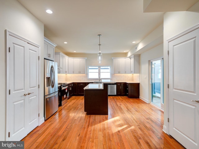 kitchen with pendant lighting, decorative backsplash, light wood-type flooring, a kitchen island, and stainless steel appliances