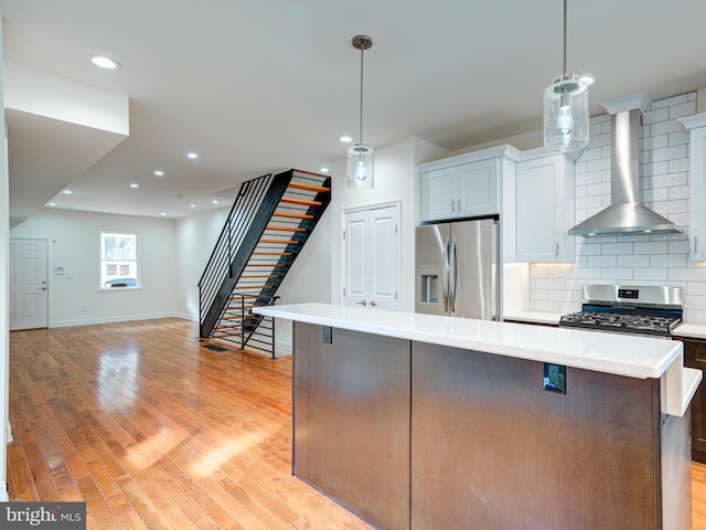 kitchen with tasteful backsplash, decorative light fixtures, stainless steel appliances, and wall chimney range hood