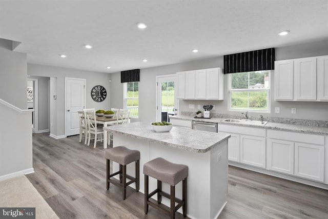 kitchen featuring light wood-type flooring, sink, dishwasher, white cabinets, and a center island