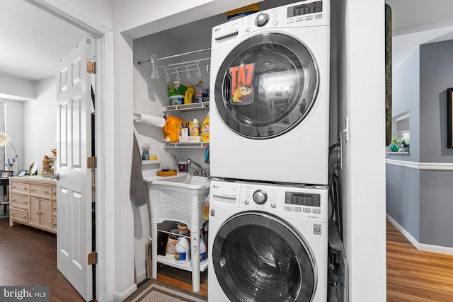 laundry area featuring dark hardwood / wood-style flooring, stacked washer and clothes dryer, and sink