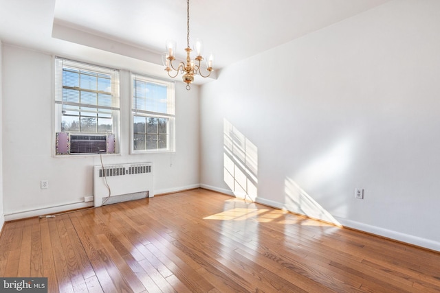 empty room with radiator, cooling unit, an inviting chandelier, and hardwood / wood-style flooring