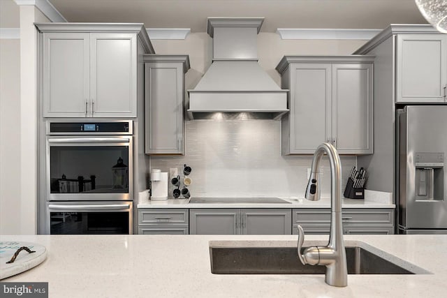 kitchen featuring custom range hood, sink, gray cabinets, decorative backsplash, and stainless steel appliances