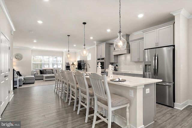 kitchen with appliances with stainless steel finishes, hanging light fixtures, a kitchen island with sink, gray cabinetry, and a breakfast bar