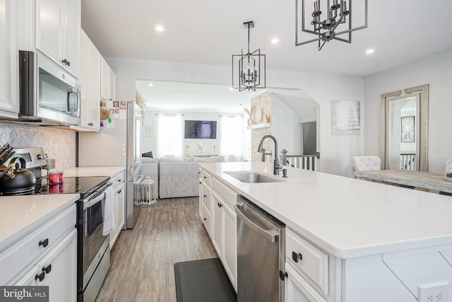 kitchen featuring appliances with stainless steel finishes, decorative light fixtures, an inviting chandelier, white cabinets, and an island with sink