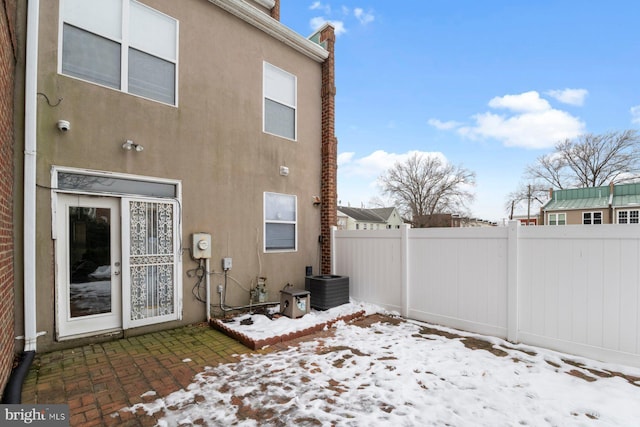 snow covered back of property featuring central air condition unit and a patio area